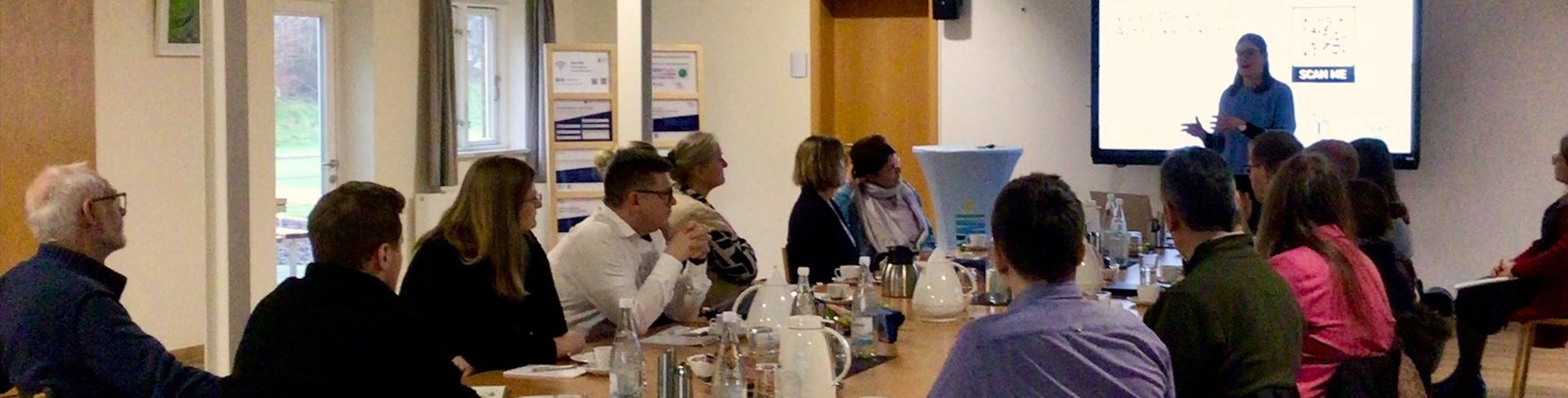 Menschen sitzen an einem Tisch und hören Vortrag