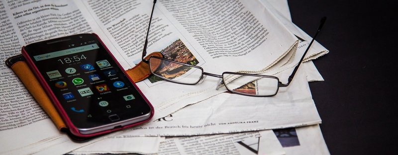 Handy und Brille liegen auf einem Stapel Zeitungen