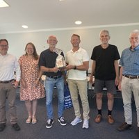 Sechs Personen stehen in Reihe und einer hat ein Präsent erhalten